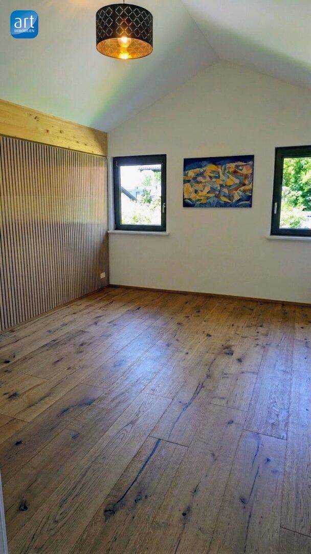 Helles Schlafzimmer mit Holzboden, schräger Decke und dekorativer Holzvertäfelung an einer Wand.