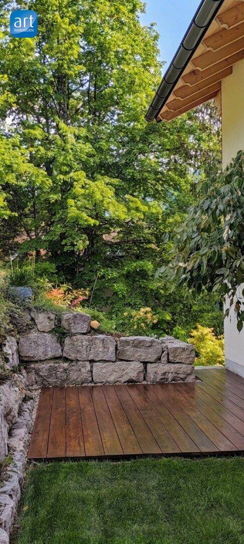 Kleine Holzterrasse umgeben von Natur und einer Steinmauer, ideal zum Entspannen.