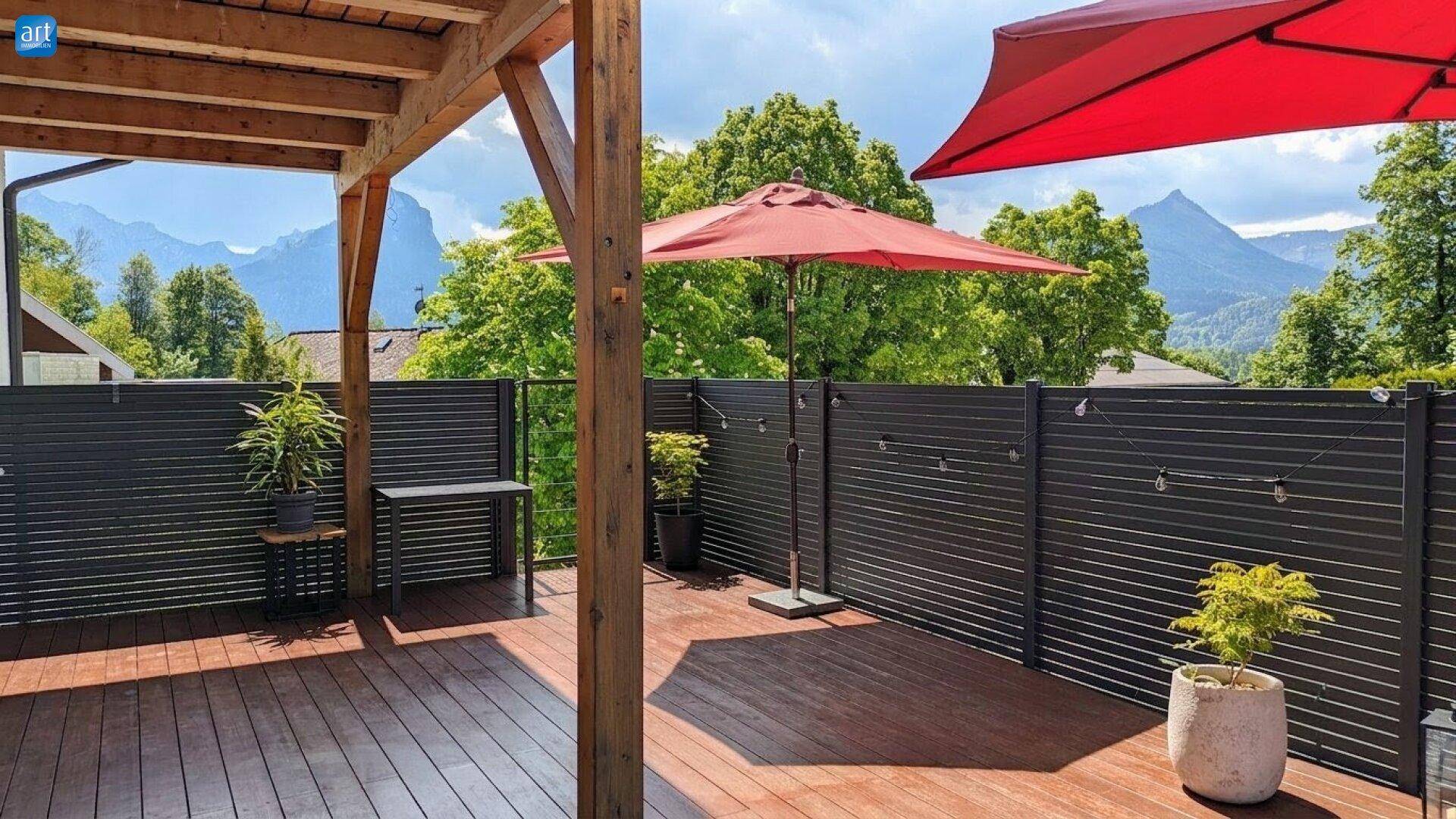 Große Holzterrasse mit Sonnenschirmen und Bergblick, umgeben von grünen Bäumen.