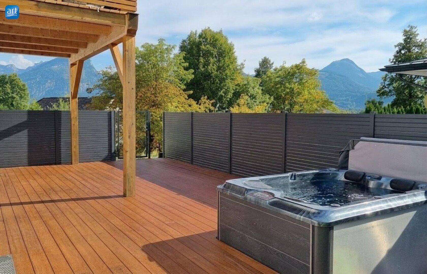 Geräumige Holzterrasse mit Whirlpool und Bergblick, umgeben von grüner Landschaft.