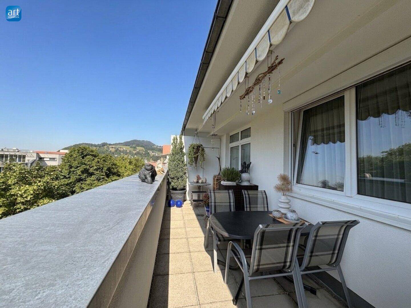 Langer Balkon mit Fliesenboden, Gartenmöbeln und Markise, ideal für sonnige Tage im Freien.