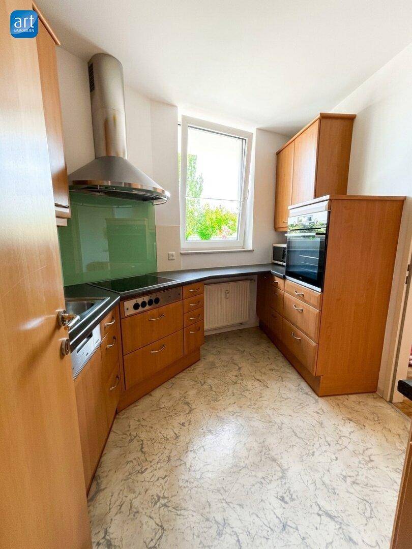 Funktionale Küche mit Holzschränken, Einbaugeräten und Fenster für natürliches Tageslicht.