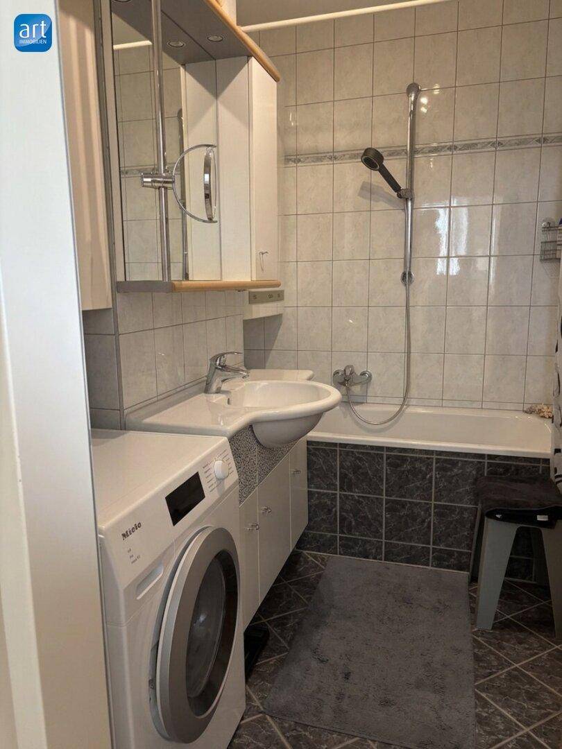 Badezimmer mit Badewanne, Dusche, Waschbecken und integrierter Waschmaschine der Marke Miele.