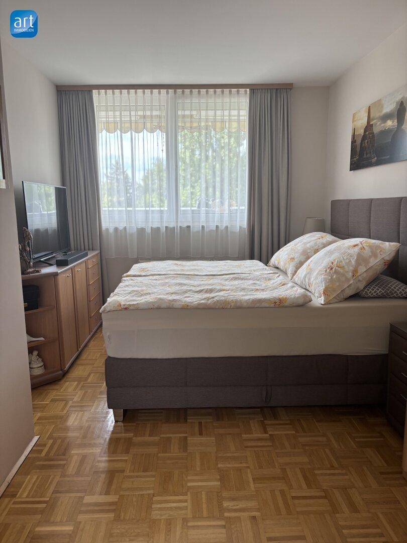 Gemütliches Schlafzimmer mit Parkettboden, großem Bett und Fenster mit Blick ins Grüne.
