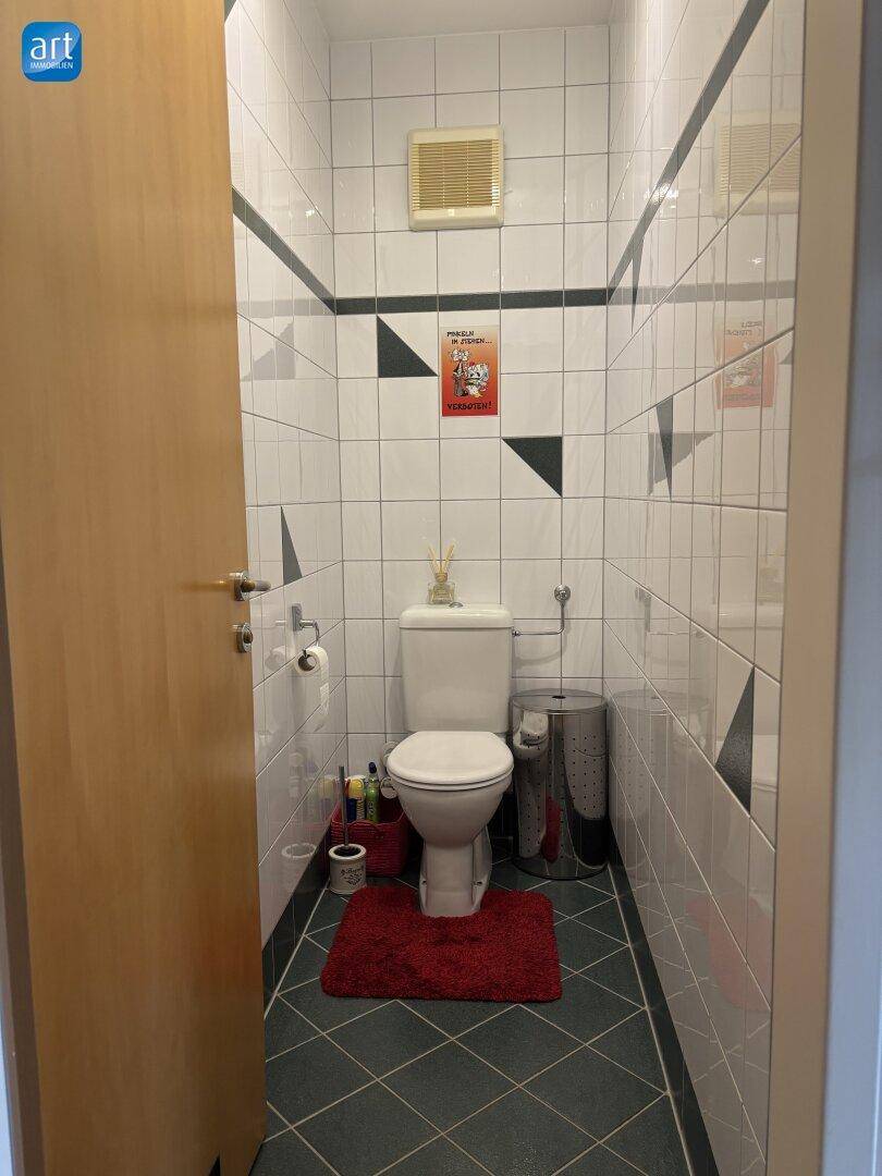 Separates WC mit Fliesenboden, Toilette und Lüftung, in einem modernen und sauberen Design.