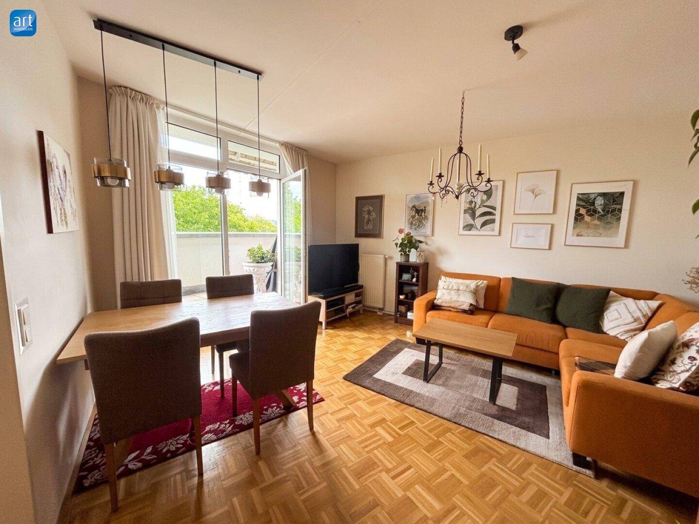 Gemütlicher Wohn-Essbereich mit Parkettboden, orangefarbenem Sofa und Zugang zum Balkon.