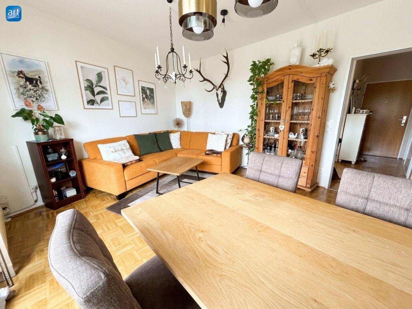 Heller Wohn-Essbereich mit Holztisch, Ecksofa und traditioneller Hirschgeweih-Dekoration an der Wand.