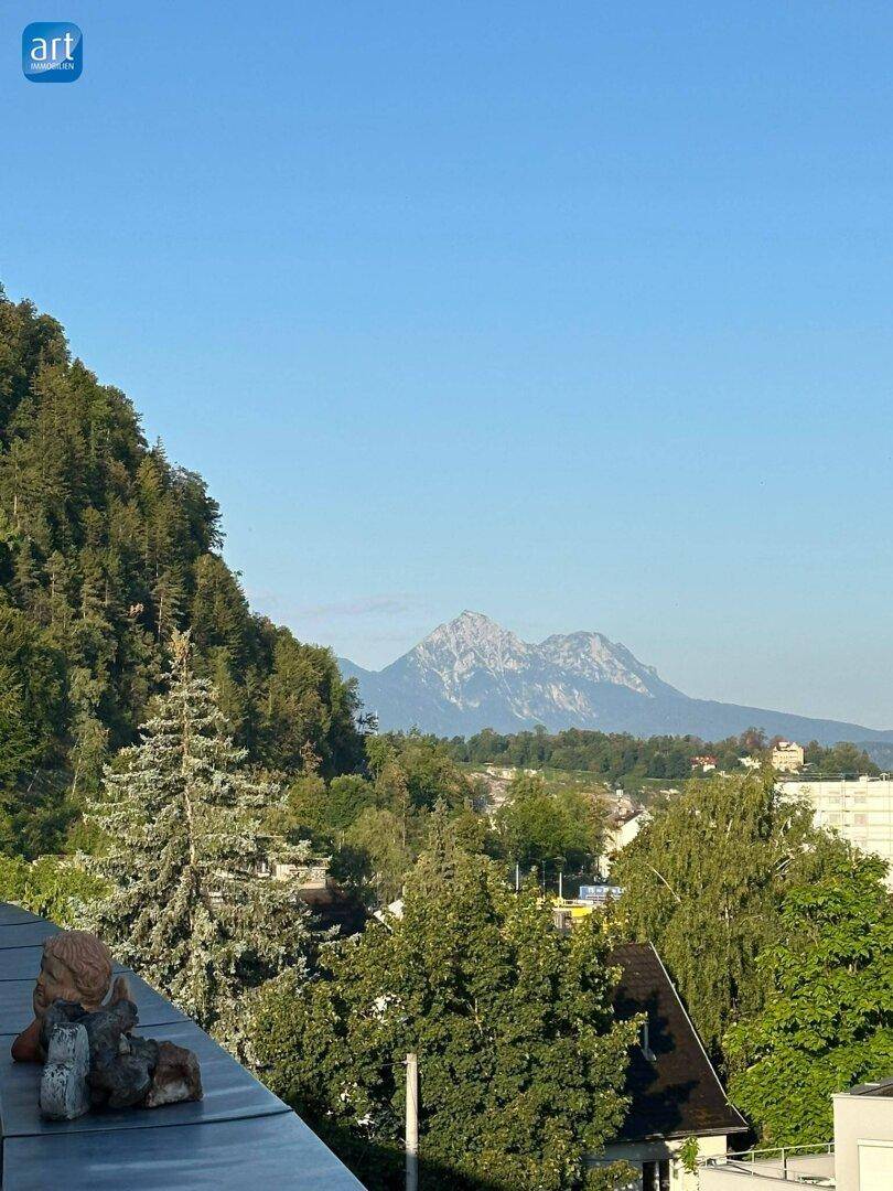Panoramablick von einem Balkon auf bewaldete Hügel und ferne Berge unter klarem blauem Himmel.