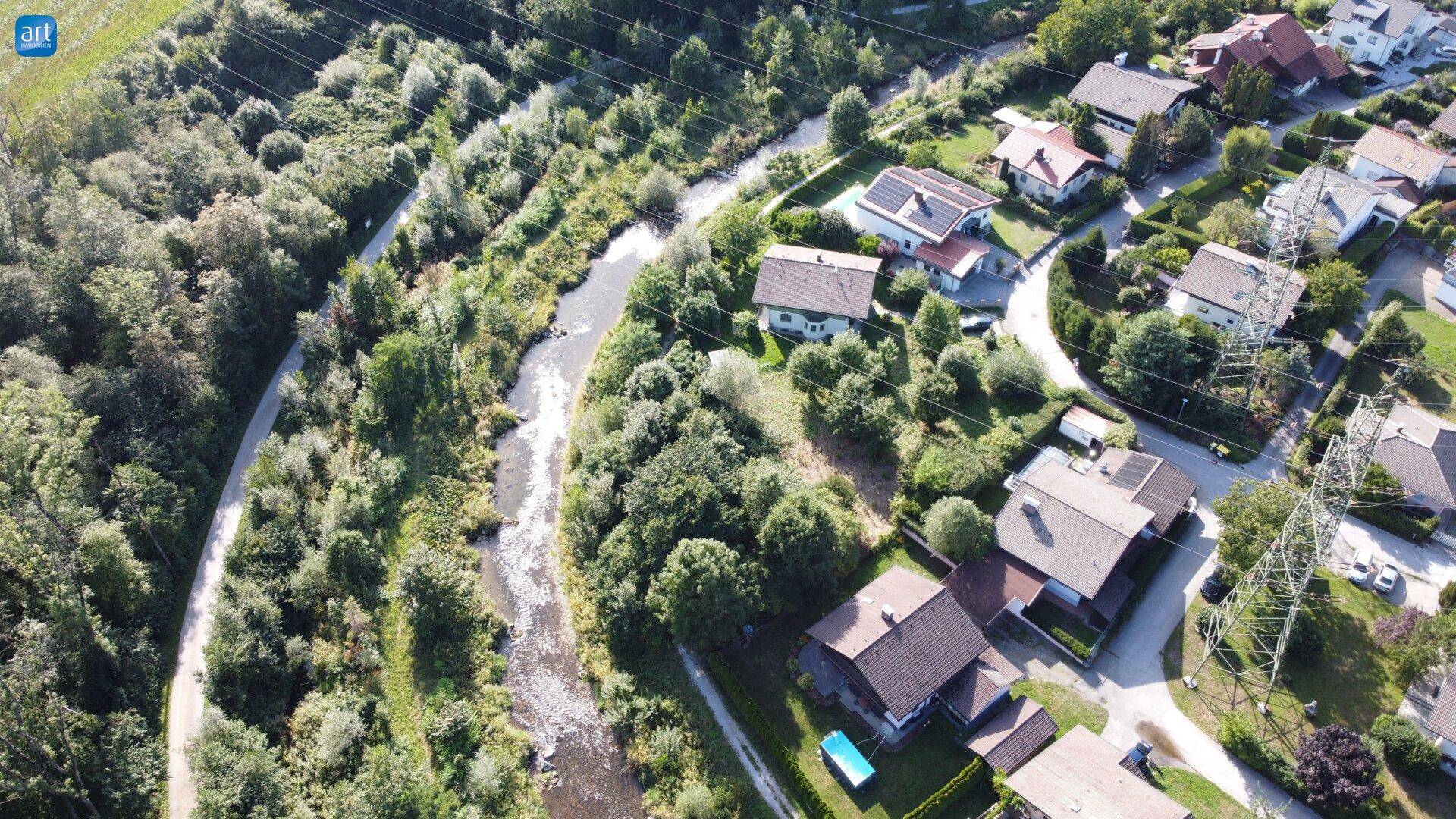 Weitläufige Luftaufnahme einer grünen Wohngegend mit einem Fluss und Strommasten.