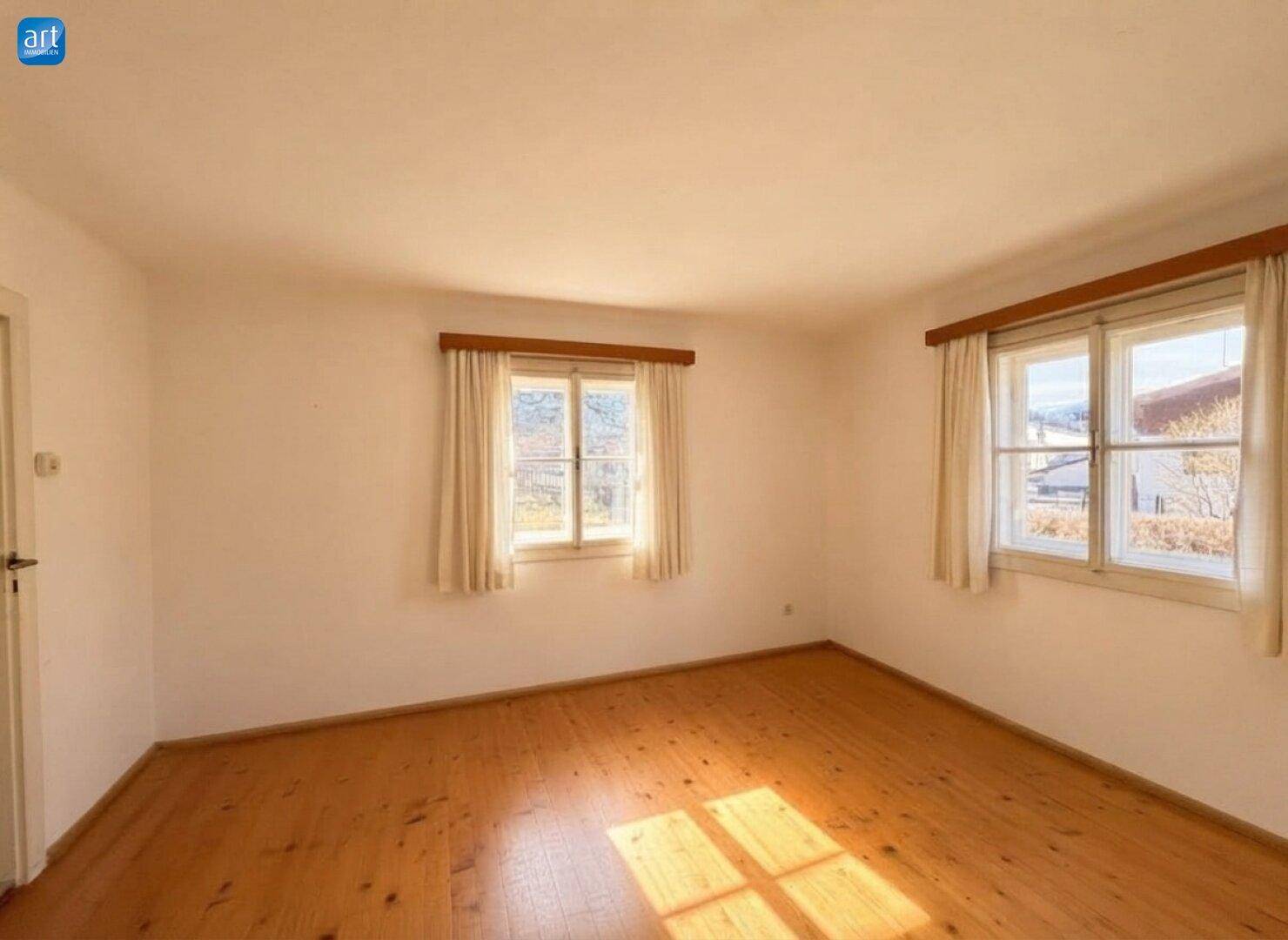 Helles Schlafzimmer mit Holzdielenboden und zwei Fenstern, die viel Licht hereinlassen.