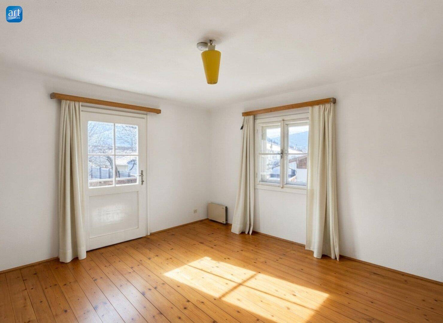 Lichtdurchflutetes Zimmer mit Holzdielenboden und Zugang zu einem Außenbereich.