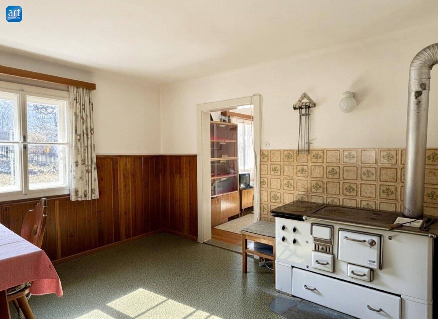 Traditionelle Küche mit Holzofen, gefliestem Bereich und Blick in einen Nebenraum.