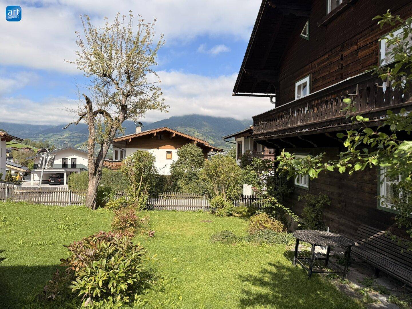 Grüner Gartenbereich mit Rasen, Bäumen und Blick auf die umliegenden Berge.