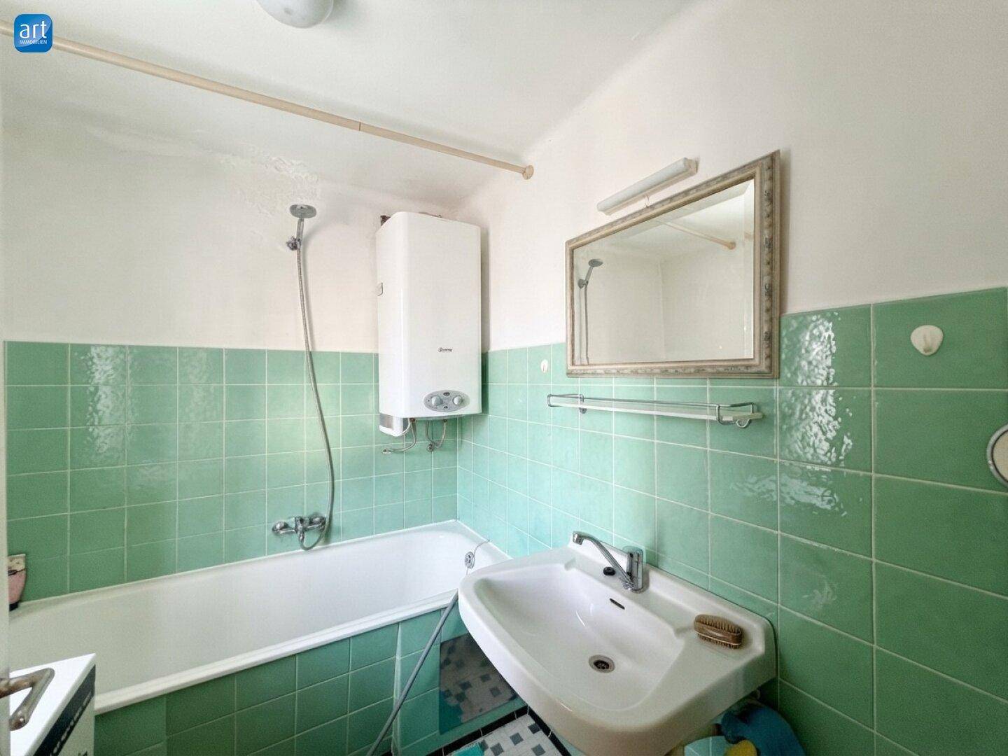 Badezimmer mit grünen Fliesen, Badewanne und Waschbecken in älterem Zustand.