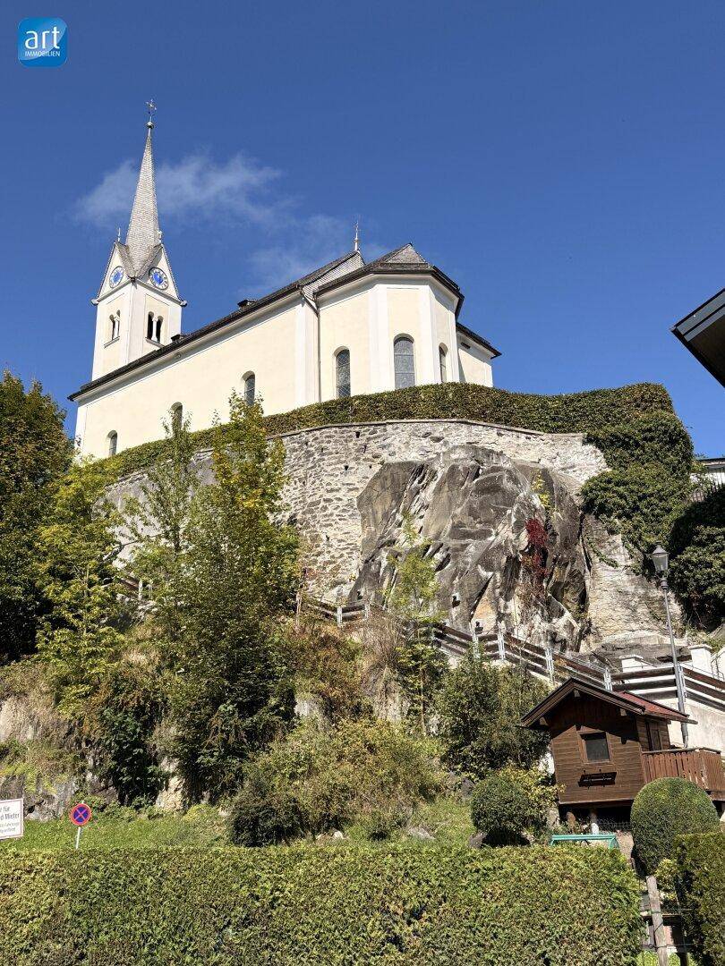 Historische Kirche auf einem Hügel mit steinerner Mauer und üppiger Vegetation.