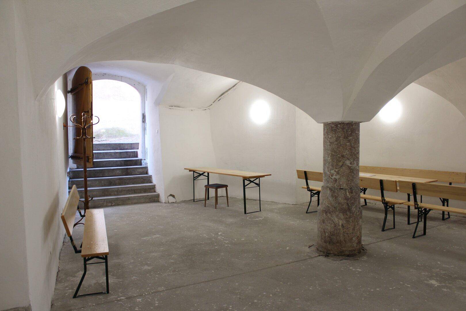 Großer Kellerraum mit beeindruckendem Tonnengewölbe, Steinpfeiler und rustikalen Holzbänken, ideal für Veranstaltungen.