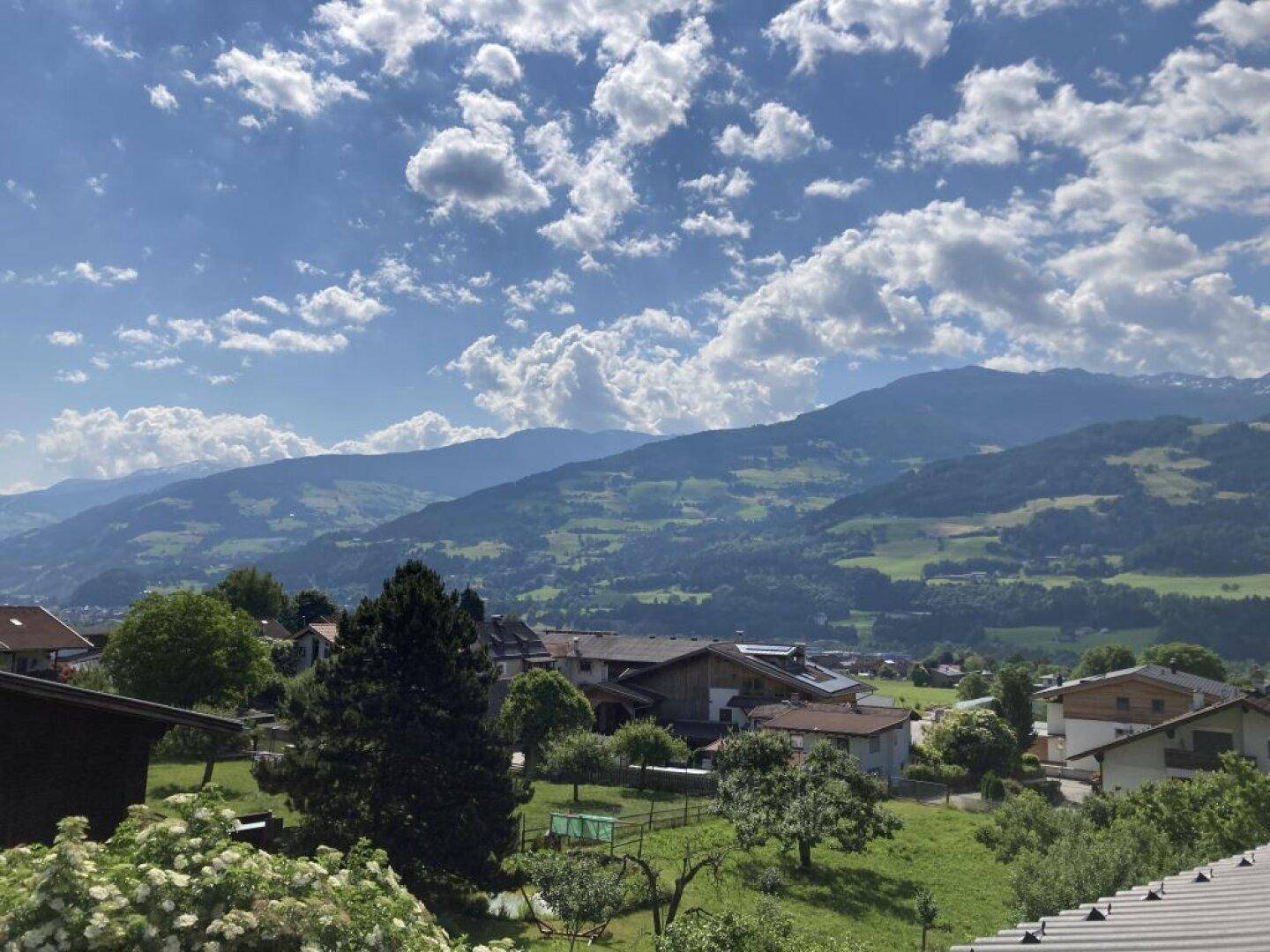 Weitläufiger Blick auf grüne Hügel und Berge unter einem blauen Himmel mit weißen Wolken.