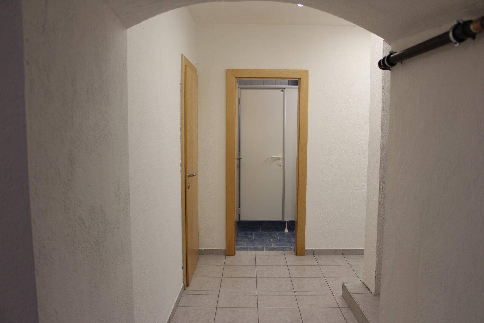 Heller Flur mit Fliesenboden und mehreren Türen, führt zu weiteren Räumen im Gebäude, sauber und funktional.