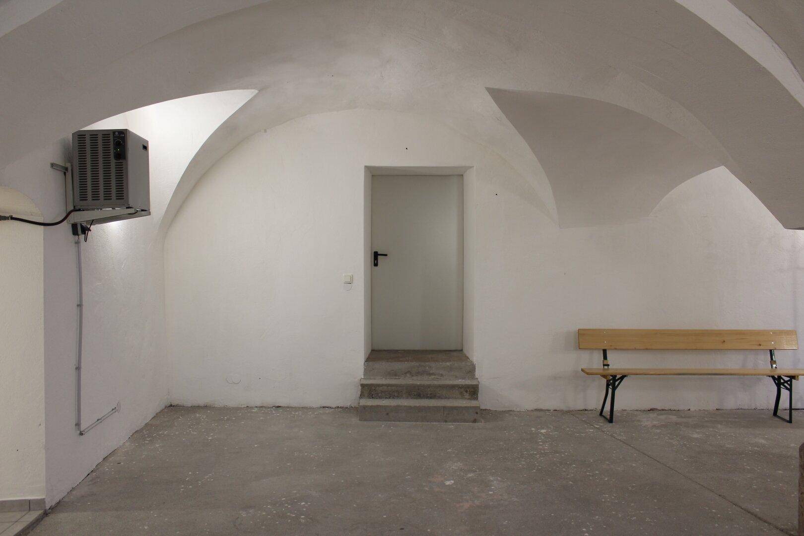 Kellerraum mit gewölbter Decke, einer Bank und einer Klimaanlage an der Wand, sauber und funktional eingerichtet.