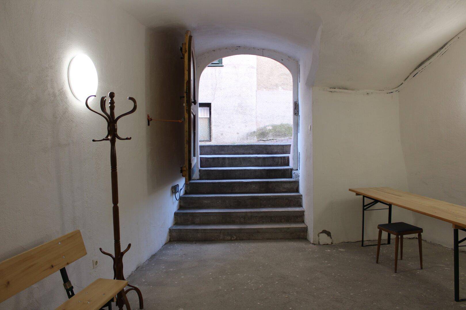 Eingangsbereich zum Keller mit Treppe, Garderobe und Holztisch, unter einer gewölbten Decke, hell und einladend.