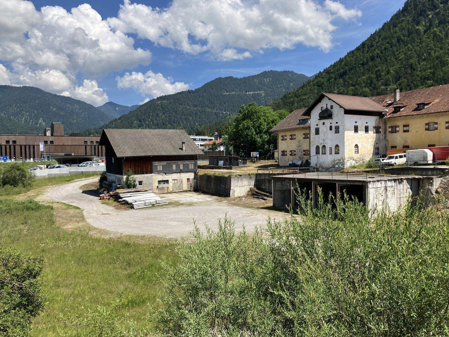 Panoramablick auf ein weitläufiges Grundstück mit mehreren Gebäuden und einer malerischen Berglandschaft im Hintergrund.
