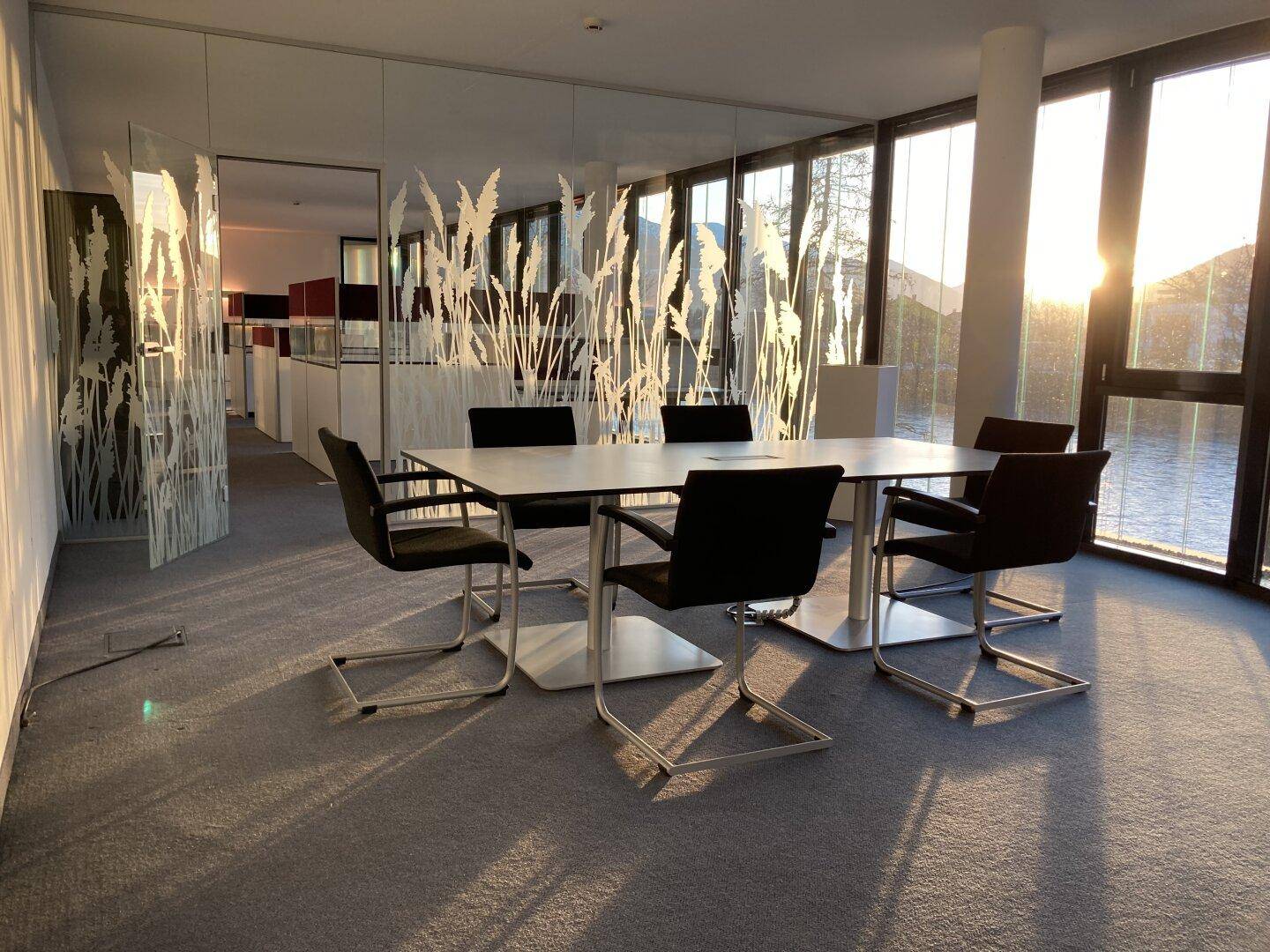Moderner Konferenzraum mit Teppichboden, großen Fenstern und Blick auf die Landschaft bei Sonnenuntergang.