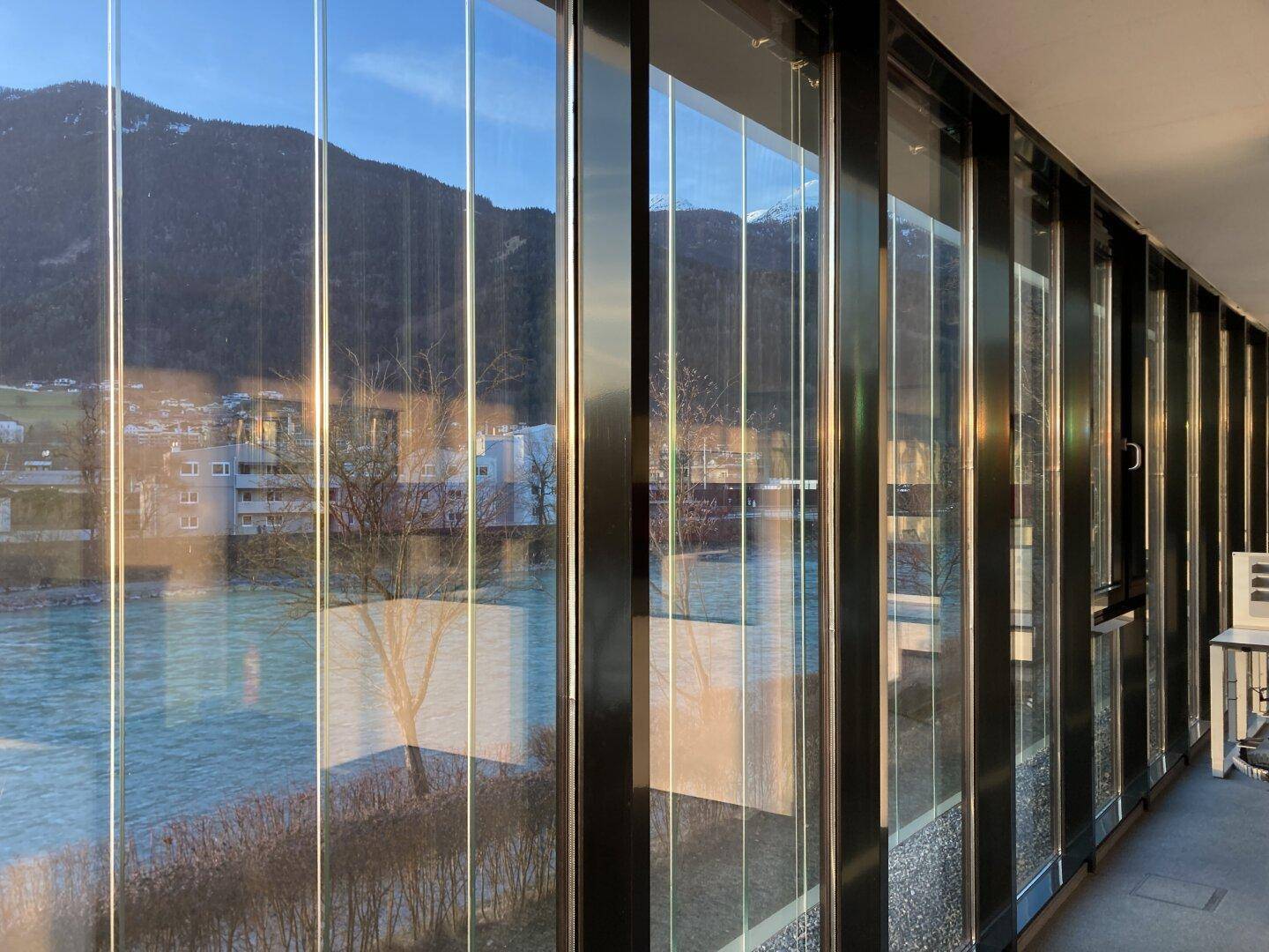 Panoramafenster bieten einen weiten Blick auf den Fluss und die gegenüberliegenden Berge bei Sonnenuntergang.