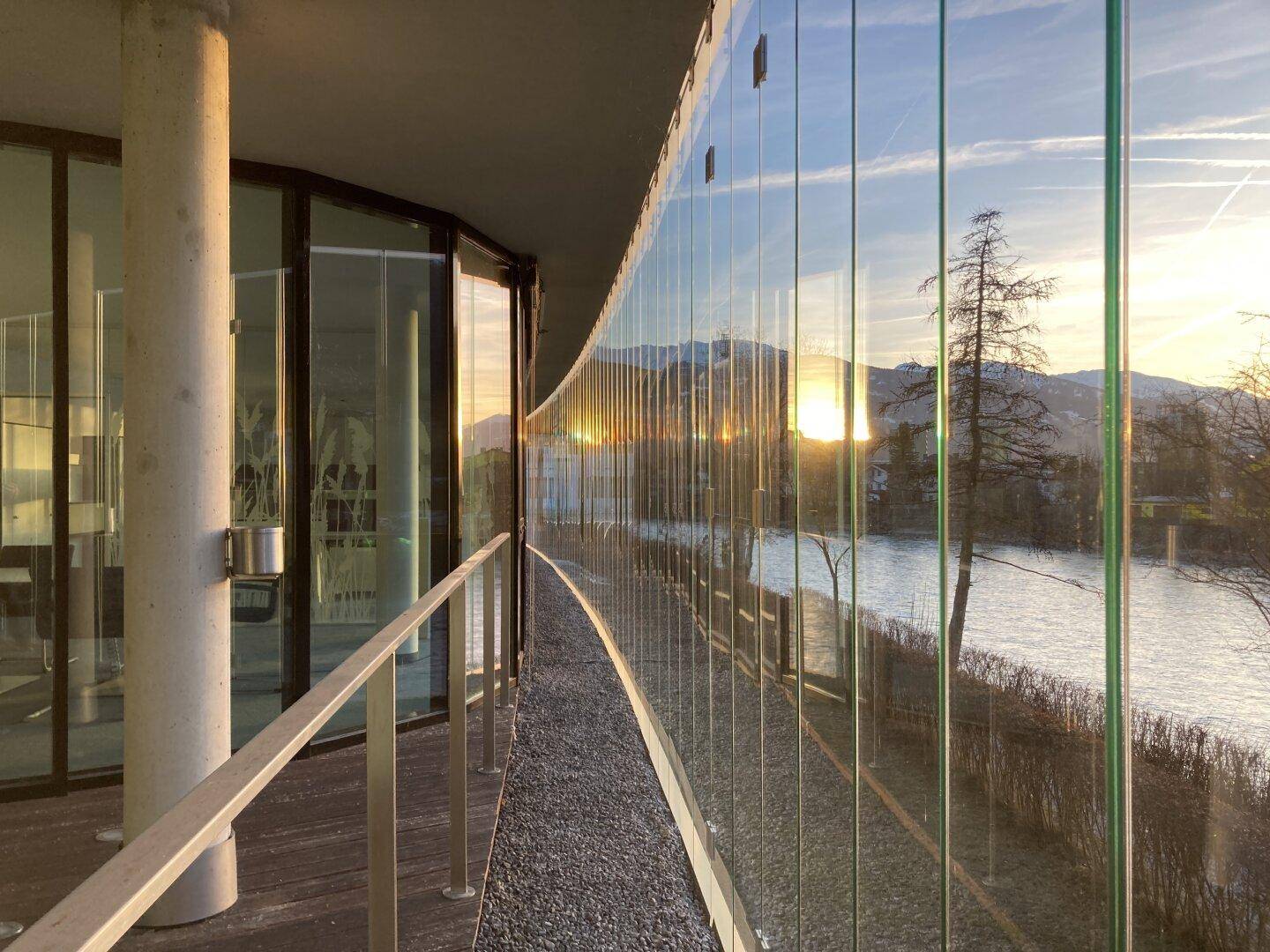 Geschwungener Balkon mit Glasbrüstung und weitem Blick auf den Fluss und die umliegende Berglandschaft.