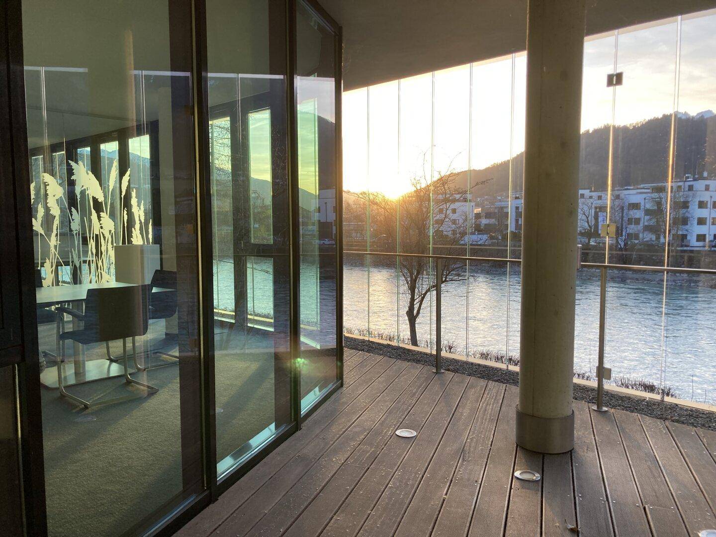 Geräumige Terrasse mit Holzboden und beeindruckendem Blick auf den Fluss und die Berge bei Sonnenuntergang.