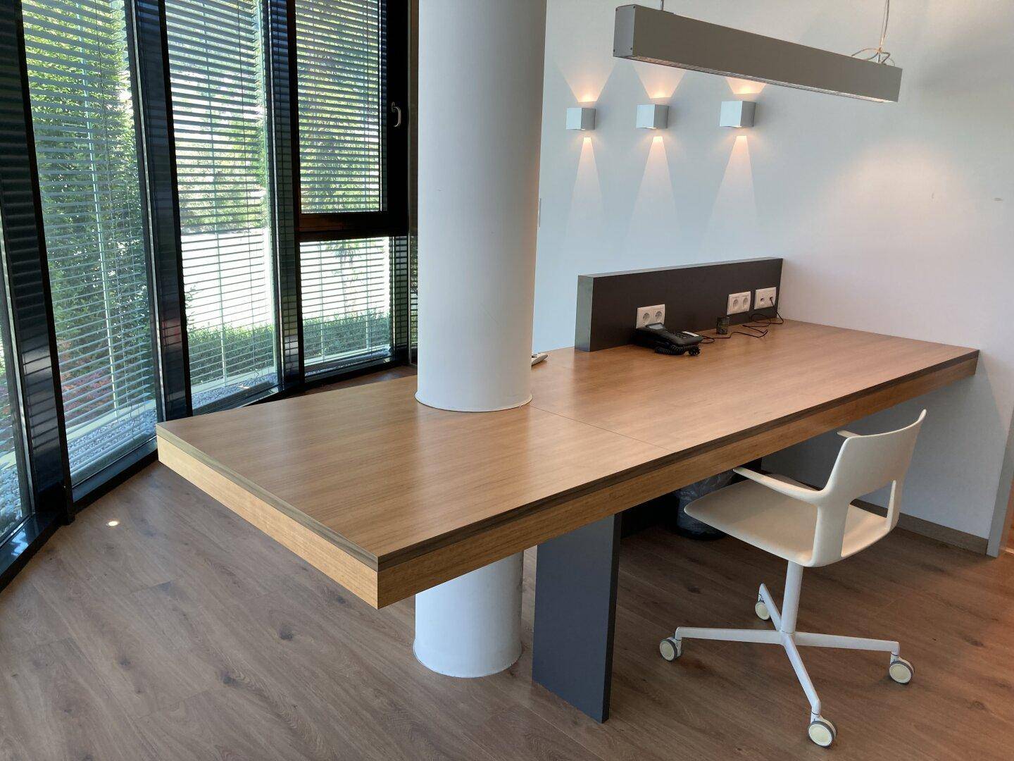 Heller Bürobereich mit modernem Schreibtisch, ergonomischem Stuhl und großen Fenstern für viel Tageslicht.