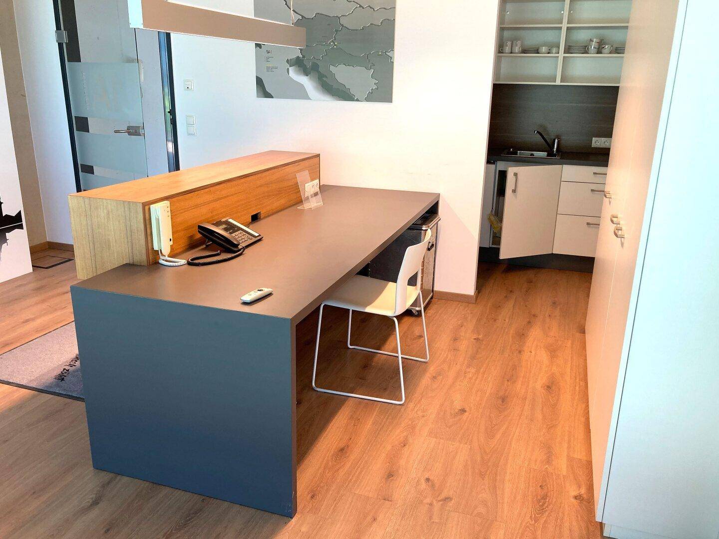 Empfangsbereich mit modernem Schreibtisch und einer kleinen, funktionalen Küchenzeile im Hintergrund.