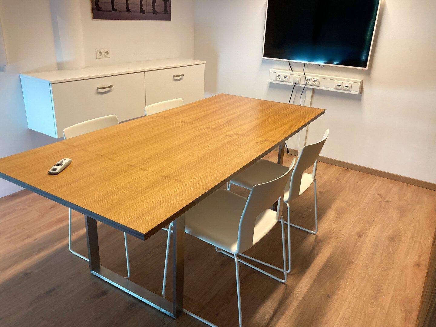 Besprechungsraum mit Holztisch, modernen Stühlen und einem an der Wand montierten Fernseher für Präsentationen.