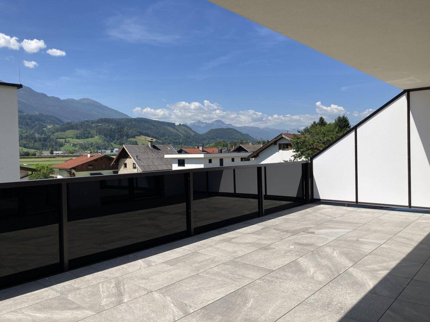 Sonniger Balkon mit weitem Ausblick über die Dächer und die majestätischen Berge im Hintergrund.