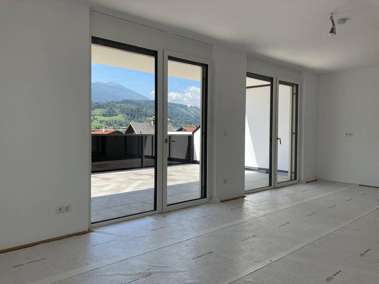 Heller Wohnraum mit großen Fensterfronten und direktem Zugang zu einem sonnigen Balkon mit Bergblick.