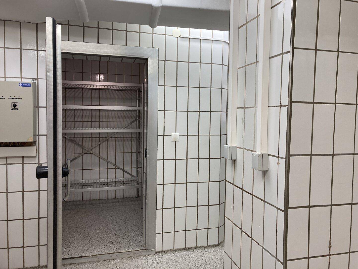 Begehbarer Kühlraum mit Metallregalen und weißen Fliesenwänden in einer Gewerbeküche.