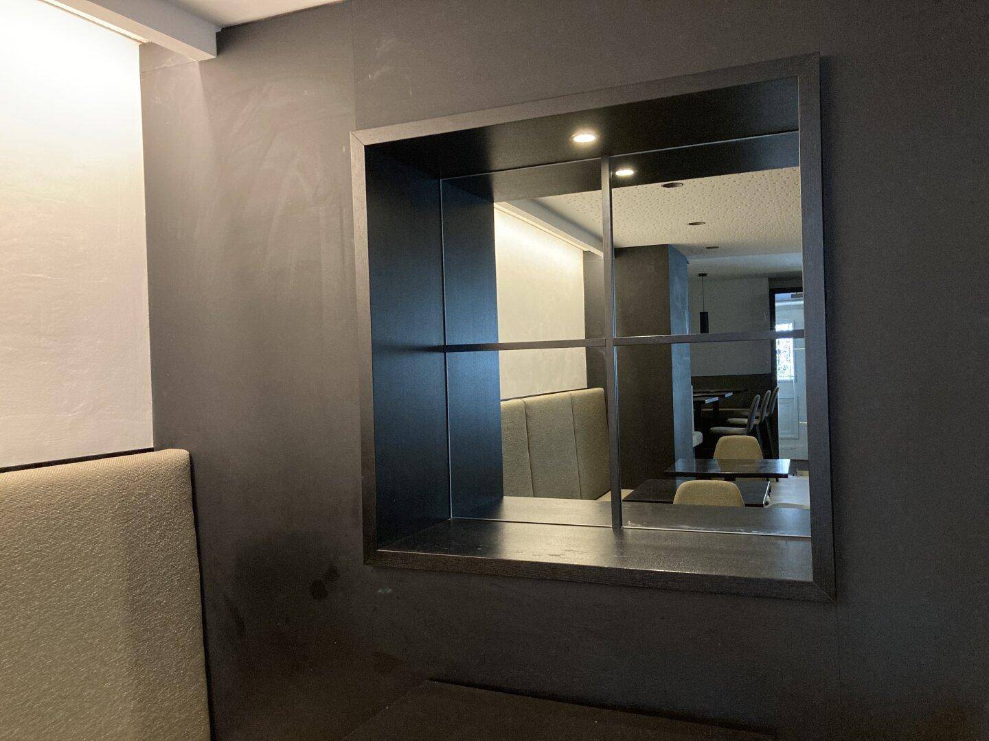 Dekoratives Spiegelelement an einer dunklen Wand, das Teile des modernen Innenraums reflektiert.