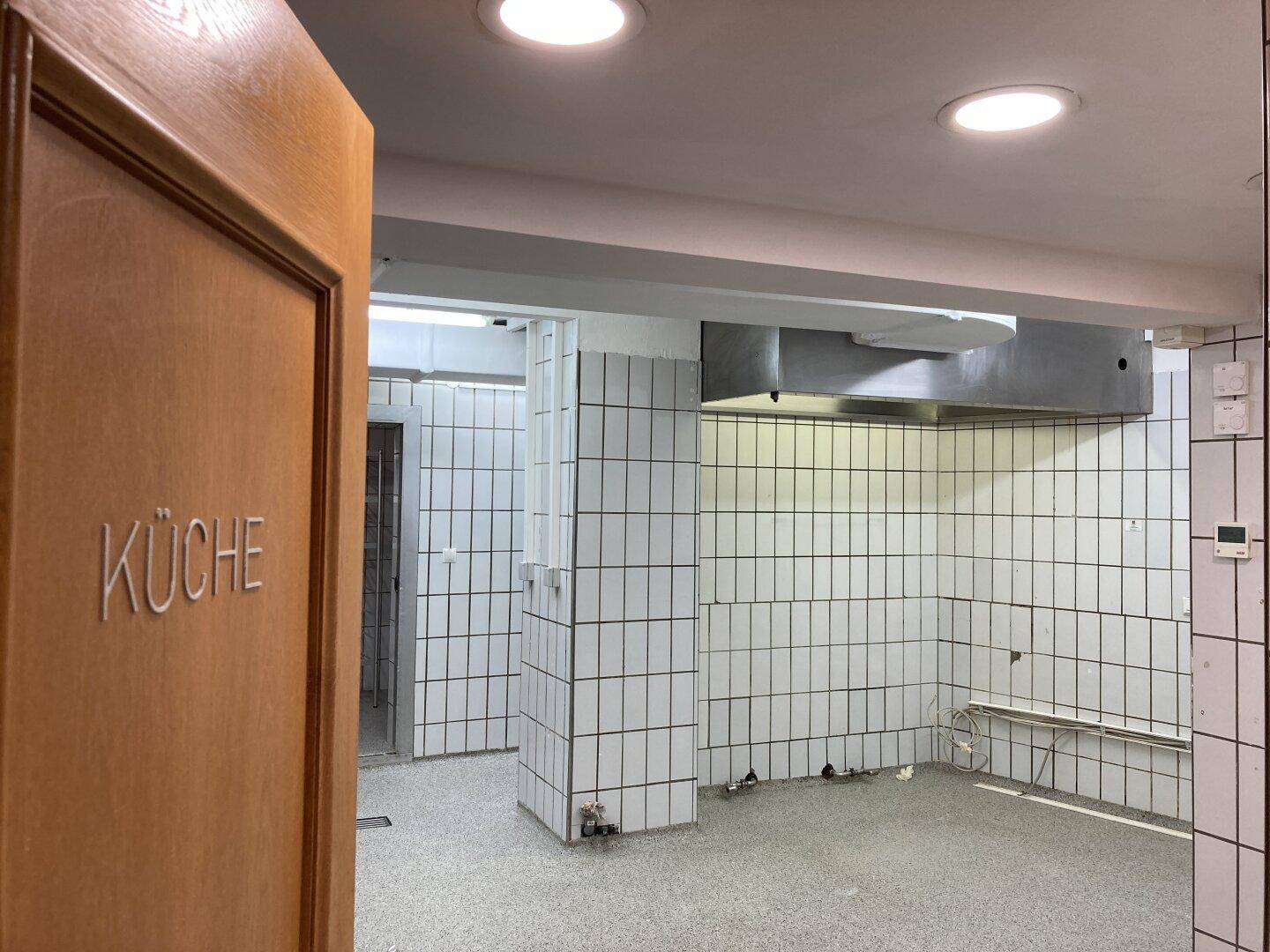 Gewerbliche Küche mit weißen Fliesenwänden, Edelstahl-Dunstabzugshaube und hellem Boden.