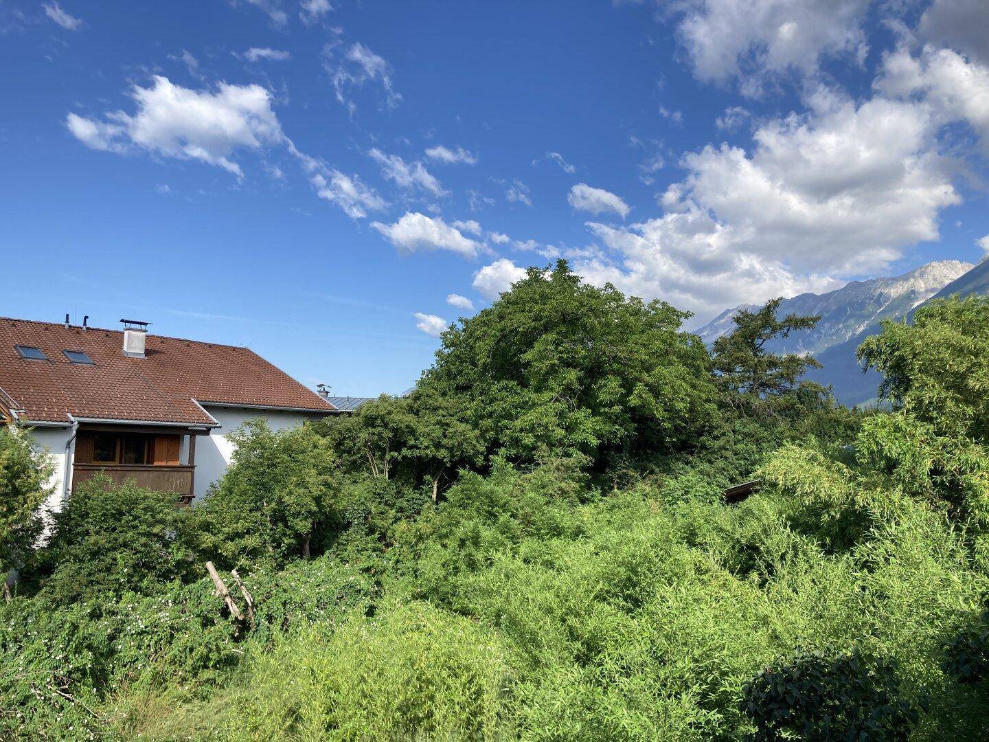 Haus mit braunem Ziegeldach und kleinem Holzbalkon, umgeben von grüner Natur und Bergblick.