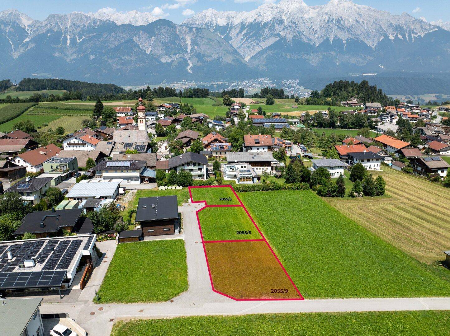 Weitläufige Luftaufnahme von Baugrundstücken mit einem Dorf und majestätischen Bergen im Hintergrund.