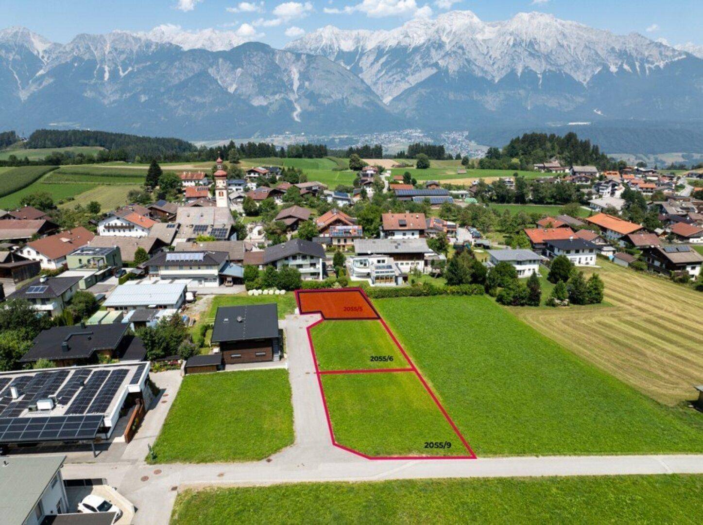 Panoramische Luftaufnahme von Baugrundstücken mit Dorf und majestätischer Bergkulisse im Hintergrund.