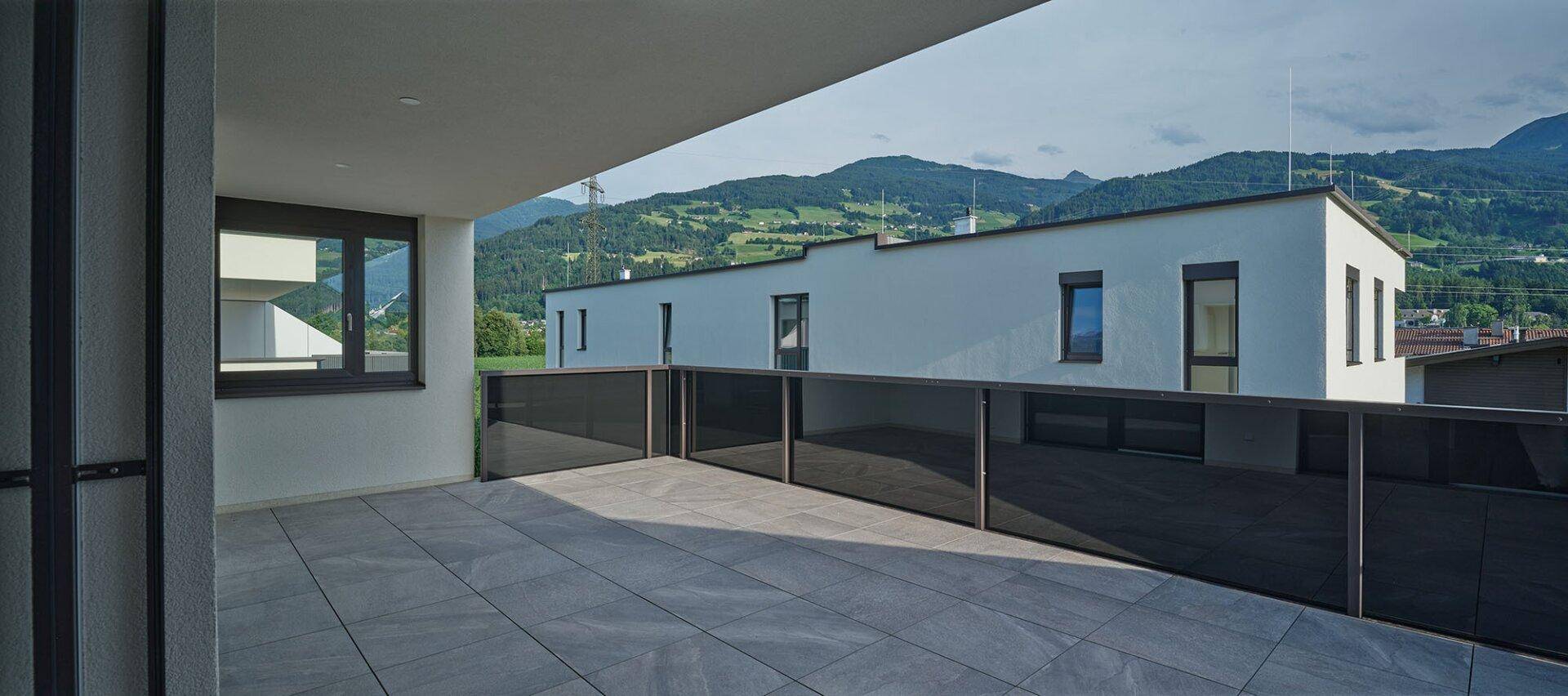Geräumige Terrasse mit Fliesenboden und Blick auf die umliegende grüne Hügellandschaft.