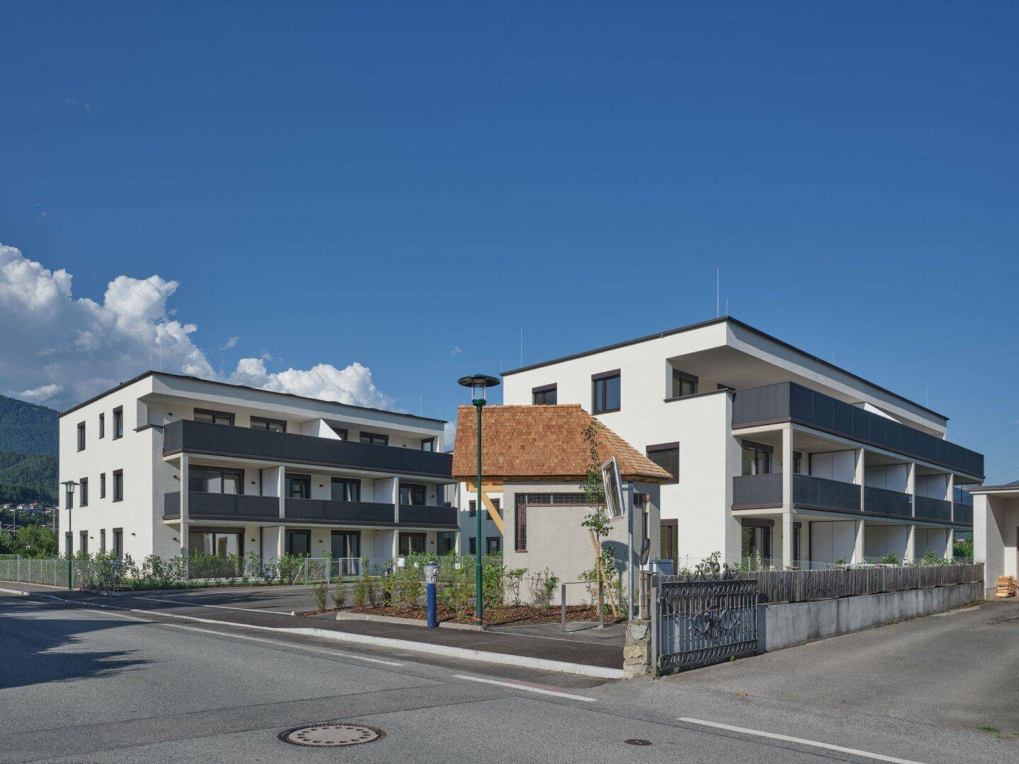 Zwei moderne Wohngebäude mit Balkonen und Flachdächern an einer ruhigen Straße gelegen.
