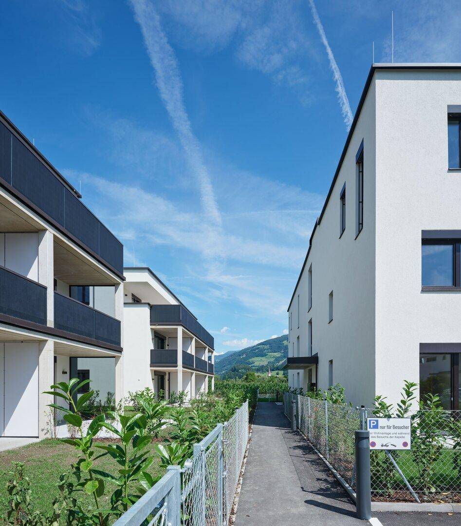 Moderne Wohngebäude mit klaren Linien und Balkonen, umgeben von grüner Landschaft und Bergen.