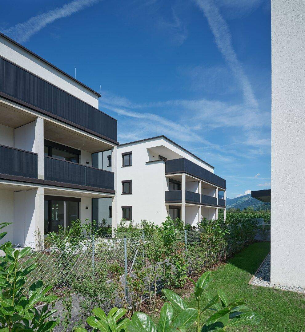 Architektur moderner Wohngebäude mit Balkonen und gepflegter Grünanlage vor Bergkulisse.