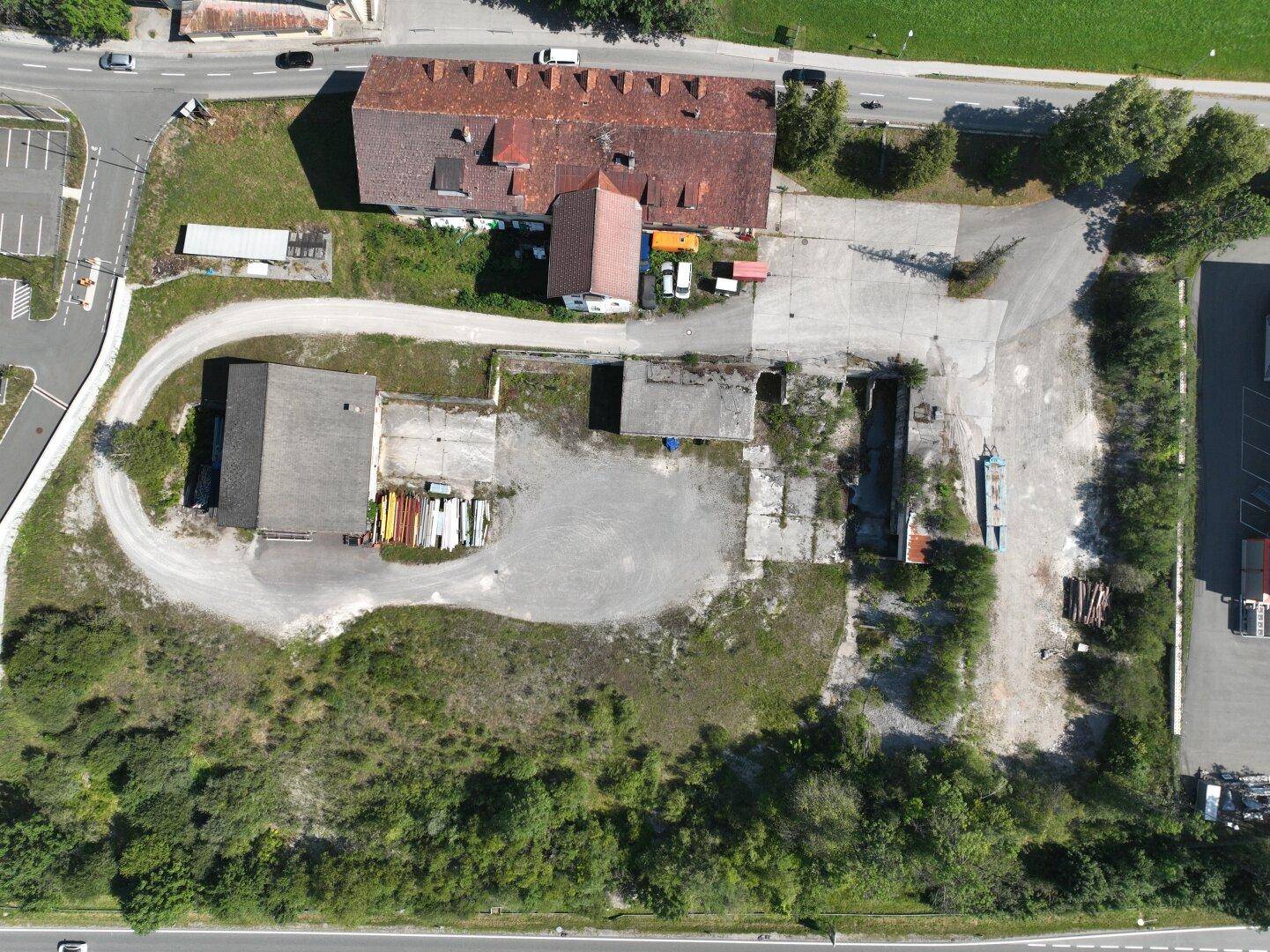 Luftaufnahme eines weitläufigen Grundstücks mit mehreren Gebäuden, unbefestigten Flächen und angrenzenden Straßen.