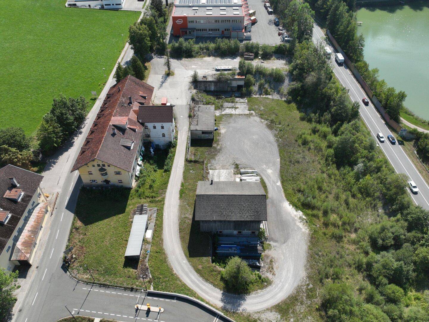 Weitläufige Luftaufnahme des Grundstücks mit angrenzender Straße und einem Gewässer im Hintergrund.