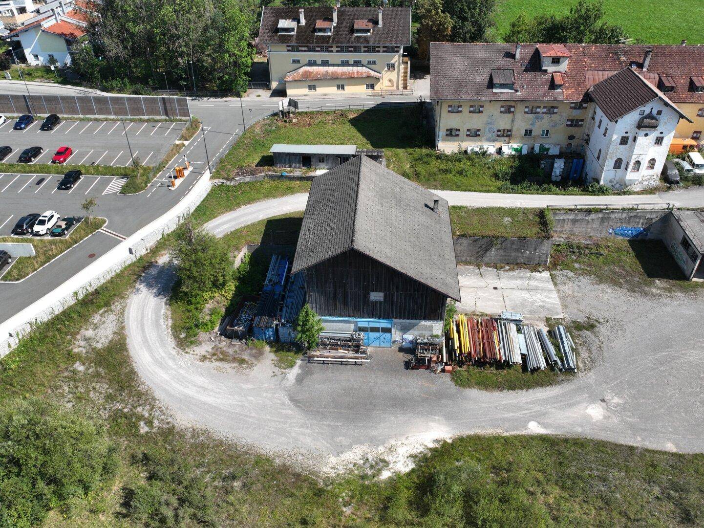 Luftaufnahme eines älteren Gebäudes mit Satteldach, umgeben von unbefestigten Flächen und gelagerten Materialien.