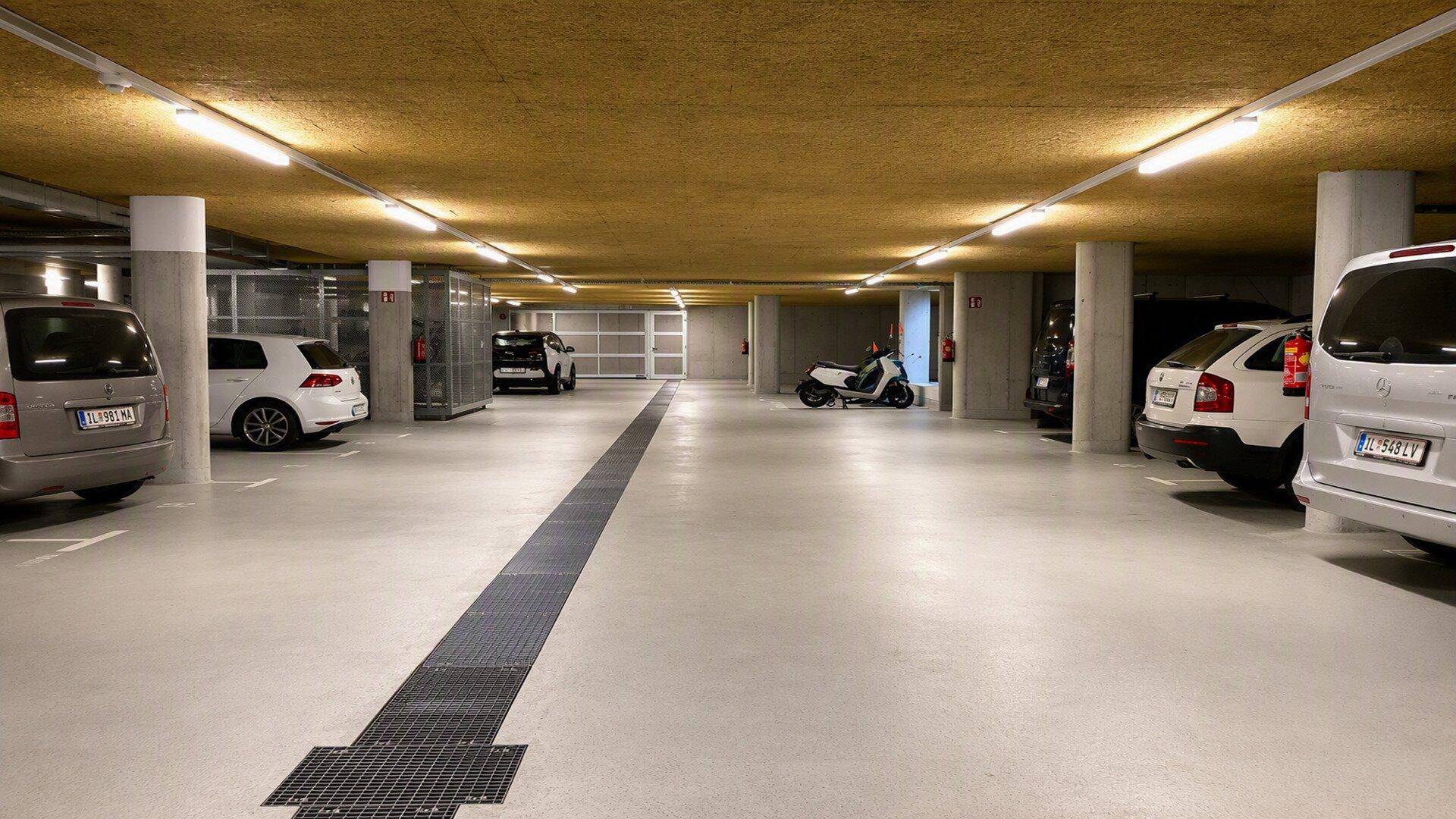 Geräumige Tiefgarage mit mehreren Stellplätzen, heller Beleuchtung und strukturierter Decke.