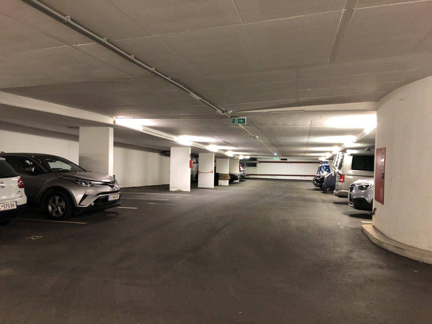 Geräumige Tiefgarage mit mehreren geparkten Fahrzeugen und Betonstützen.