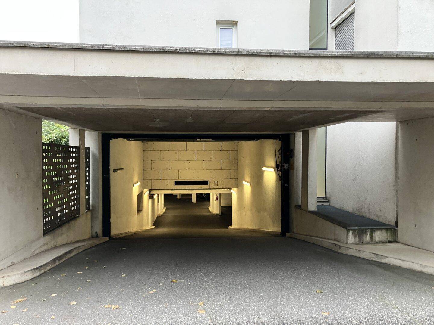 Einfahrt zu einer Tiefgarage unter einem modernen Gebäude mit Rampe und perforierter Wand.